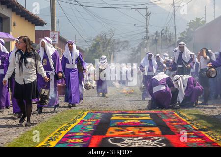 Semana-Santa-Teilnehmer mit Weihrauch neben einer farbenfrohen Sägespanalmatte während einer Prozession in der Heiligen Woche in Antigua Guatemala. Stockfoto