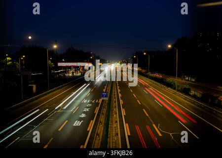 Langzeitbelichtung von nächtlichen Verkehrsleuchten auf einer Hochstraße mit Mond Stockfoto
