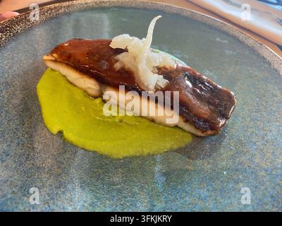 Gegrilltes Seebassfilet auf einem modernen Teller mit lebhaftem Erbsenpüree und eingelegtem Gemüse, angerichtet für feine Küche, elegante, frische Meeresfrüchtepräsentation für Stockfoto