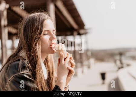 Frau, die Eiscreme isst, junge Frau genießt ein köstliches rosa Eiswaffel im Freien im warmen Sonnenlicht mit Kopierraum Stockfoto