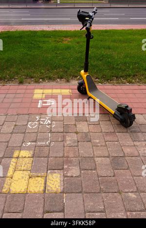 Gelber Elektroscooter, der in einem ausgewiesenen Parkbereich geparkt ist. Urbane Infrastruktur für organisiertes alternatives Transportkonzept Stockfoto