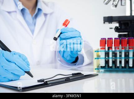 Arzt nimmt eine Blutprobe aus einem Rack mit Analysegeräten im Laborhintergrund. Techniker hält ein Blutprobenröhrchen in der Forschung Stockfoto