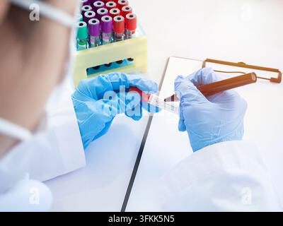 Arzt nimmt eine Blutprobe aus einem Rack mit Analysegeräten im Labor, Techniker hält ein Blutprobenröhrchen im Forschungslabor Stockfoto