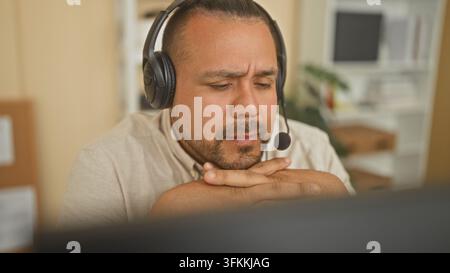 Männlicher Callcenter-Agent mit Headset ruht die Hände unter dem Kinn am Computerbildschirm im Bürogebäude; konzentrierte Besorgnis. Stockfoto