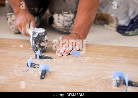 Mann montiert neue Bodenziegel mit einem Gummihammer während der Renovierung des Hauses Stockfoto