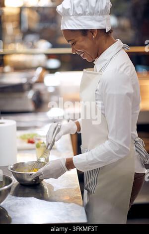 Koch in professioneller moderner Küche, Restaurantkonzept. lächelnder Koch schlägt Eier in einer Schüssel auf. Stockfoto
