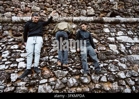 Nazare, Portugal - 6. Dezember 2025: Drei junge Männer stehen auf den Felsen in Nazare, Portugal. Stockfoto