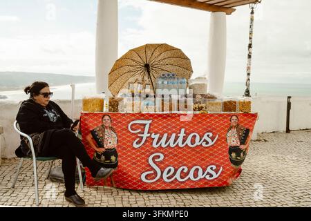 Nazare, Portugal - 7. Dezember 2025: Frau, die an ihrem Stand in Nazare, Portugal, sitzt Stockfoto