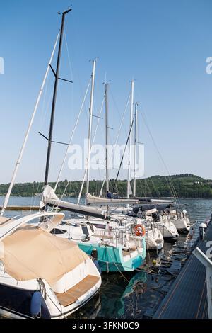 Kleine Boote und Segelboote, die neben einem Marinasteg unter einem klaren blauen Himmel vertäut sind. Friedliches Ufer und Bootsbegriff Stockfoto