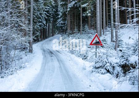 Straßenschild warnt vor einer steilen Steigung neben einer vereisten und schneebedeckten Straße in einer Winterlandschaft, wobei gefährliche Fahrbedingungen hervorgehoben werden. Stockfoto