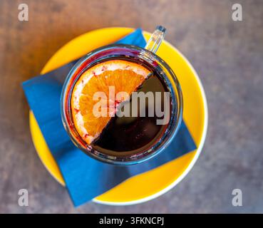 Oberansicht einer warmen Tasse Glühwein mit einer halben Orangenscheibe, die auf der Oberfläche schwimmt, platziert auf einem rustikalen Holztisch im Winter. Stockfoto