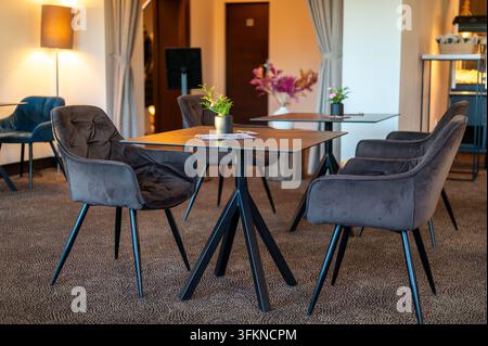 Kleine Tische, umgeben von bequemen, mit Wildleder bezogenen Sesseln in einem gemütlichen Café-Interieur, vorbereitet und wartend auf Gäste. Stockfoto