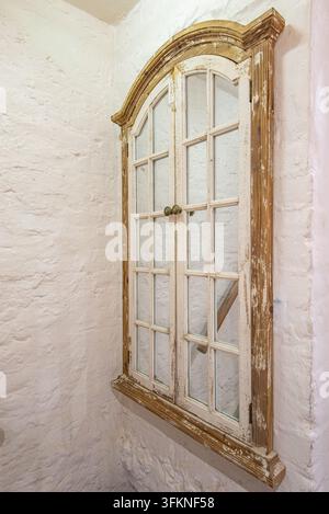 Rustischer Vintage-Spiegel mit gebogenem Fensterrahmen aus abgenutzter lackierter Holzoptik, montiert an einer strukturierten weißen Ziegelwand. Stockfoto