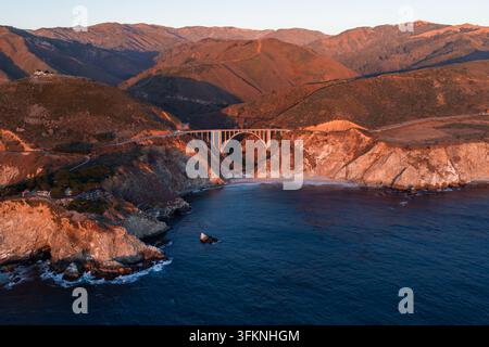 Luftbild zeigt die Bixby-Creek-Brücke, die vom Sonnenlicht des Sonnenuntergangs beleuchtet wird, entlang der Highway 1 in Big Sur, Kalifornien, die sich über ein raues Canyon neben dem Pazifik erstreckt Stockfoto