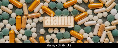 Ansicht von oben eines hölzernen Blockplatzes, der von verschiedenen Vitaminpillen und bunten Nahrungsergänzungsmittel-Kapseln auf einer dunklen Oberfläche eingerahmt ist. Stockfoto