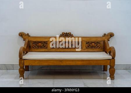 Holzsofa mit Kissen in der Nähe einer weißen Betonwand in einem leeren Wohnzimmer-Interieur, Ägypten Stockfoto