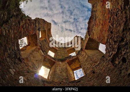 Niedriger Blick nach oben in das Innere eines kreisförmigen mittelalterlichen Steinturms, der rechteckige Fensteröffnungen, eine Sonnenlichtreflexion und einen bewölkten blauen Himmel offenbart. Stockfoto