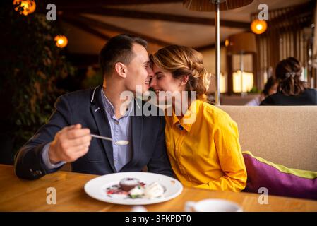 Glücklicher junger Mann füttert eine Frau mit einem Löffel ein Dessert Stockfoto