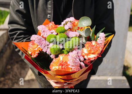 Person hält farbenfrohen Strauß mit gemischten Blumen, eingewickelt in dekoratives Papier. Floraler Hintergrund für Geschenkfeier, Romantikgruß und besonderen Anlass Stockfoto