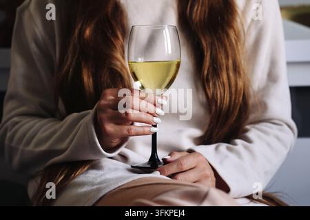 Frau hält ein Glas Weißwein und liest. Lifestyle-Hintergrund für Entspannung, Freizeit, Abendgetränk und ruhige Zeit zu Hause. Stockfoto