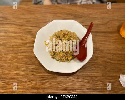 Ein Teller mit japanischem gebratenem Reis und einem roten Löffel auf einem hölzernen Restauranttisch in Japan. Stockfoto