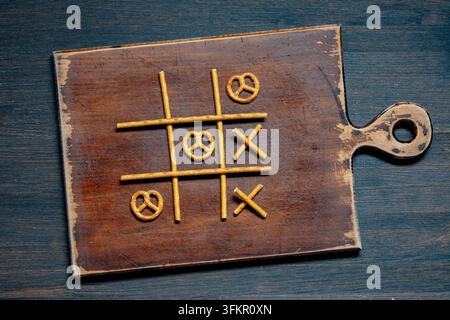 Tic-Tac-Toe-Spiel aus Brezn-Snacks, Nahaufnahme. Kreatives Tic-Tac-Toe-Spielbrett aus salzigen Brezn-Stäbchen und -Gedrehten auf rustikalem Holzschneidebrett Stockfoto