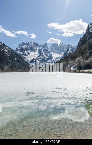 Schnee bedeckt den Landrosee in den Dolomiten im Winter. Schneebedeckte Berge erheben sich im Hintergrund unter einem klaren Himmel. Stockfoto