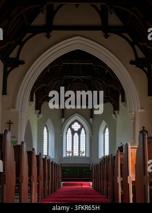 Loweswater, Vereinigtes Königreich. 20. September 2026. Das Innere einer historischen Kirche, mit Reihen von Holzbänken, die auf einen in weiches Licht getauchten Altar zuführen Stockfoto