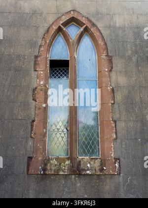 20. September 2026, Loweswater, Vereinigtes Königreich. Ein altes, gotisch stilisiertes Gewölbefenster mit diamantmusterigem Glas, eingebettet in eine verwitterte Steinmauer, evo Stockfoto