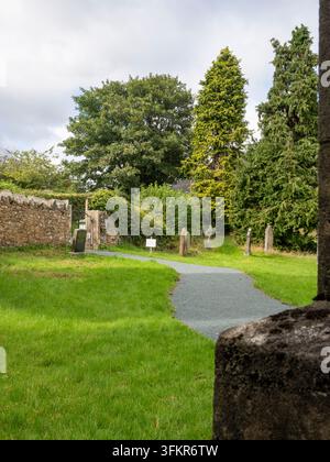 20. September 2026, Loweswater, Vereinigtes Königreich. Ein friedlicher Weg schlängelt sich durch einen üppigen grünen Kirchhof, begrenzt von alten Steinmauern und ausgewachsenen Stockfoto