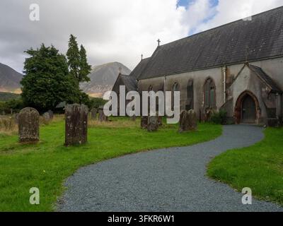 20. September 2026, Loweswater, Vereinigtes Königreich. Ein gewundener Kiesweg führt durch einen grasbewachsenen Friedhof zu einer historischen Steinkirche, mit dramatischem Stockfoto