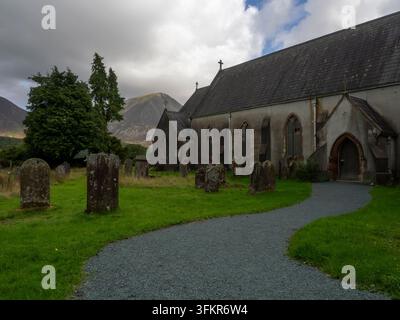 20. September 2026, Loweswater, Vereinigtes Königreich. Eine historische Kirche und ihr Friedhof stehen unter einem dramatischen, bewölkten Himmel, mit einer majestätischen Bergkette Stockfoto