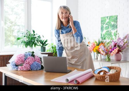 Florist mit Telefon und Laptop, der eine Bestellung im Geschäft aufnimmt Stockfoto