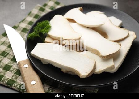 Frische Austernpilze mit Petersilie und Messer auf grauem Tisch, Nahaufnahme Stockfoto