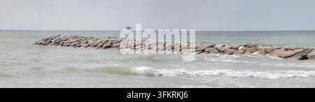 große panoramische Landschaft mit Steinbarriere an einem sandigen Adriastrand, aufgenommen im sommerlichen Hellen bei Ereaclea Mare, Veneto, Italien Stockfoto