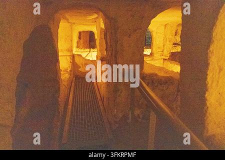 Eine stark strukturierte, warmtönige Ansicht von rauen Steinoberflächen und geschnitzten Nischen in den Katakomben von Rabat, Malta. Stockfoto