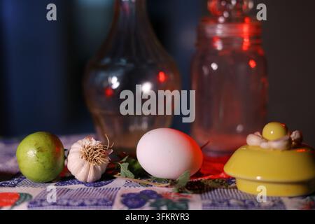 Klassisches Kätzchen-Stillleben mit frischem Ei, Knoblauch, Keramikdeckel und Glasgläsern vor dunklem, stimmungsvoller Hintergrund. Stockfoto