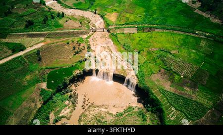 Luftbild der Matsirga-Wasserfälle mit ihrem kaskadierenden braunen Wasser, das durch üppige grüne landwirtschaftliche Felder und eine kleine Brücke in Madakiya, Kadun fließt Stockfoto