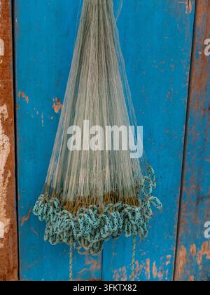 Traditionales Nylon-Angelnetz mit beschlagenen Seilkanten, das vor einer verwitterten blauen Holztür im Souq Waqif Doha hängt. Stockfoto
