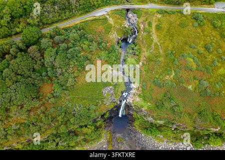 Luftaufnahme von oben eines Baches, der über mehrere Wasserfälle fließt und sich durch üppiges Farnkraut, Gras und Wald in Richtung der Küste unten schneidet Stockfoto