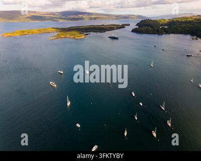 Boote und Yachten, die in ruhigen blauen Küstengewässern vor Anker liegen, bewaldete Inseln und sanfte Hügel am Horizont, Hochwinkel-Luftaufnahme Stockfoto