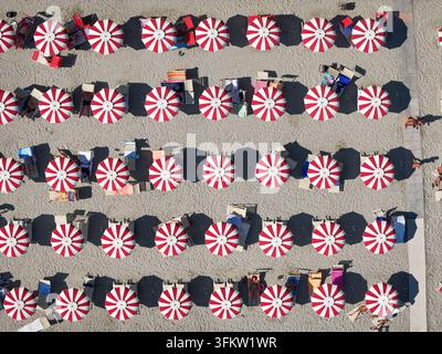 Luftaufnahme von Reihen roter und weißer gestreifter Strandschirme und Sonnenliegen auf dem Sandstrand in Bergeggi, Ligurien, Italien. Stockfoto