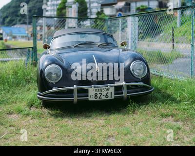 Klassischer schwarzer Porsche 356, der auf Küstengras mit Palmen in Aichi, Japan, geparkt ist Stockfoto