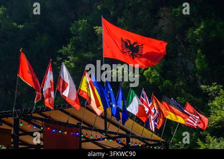 Albanische Flagge fliegt über europäischen Flaggen und Lichterketten in einer üppigen Berglandschaft Stockfoto