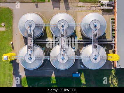 Luftaufnahme einer Kläranlage mit sechs großen runden Metalltanks, die durch Industriegänge verbunden sind, umgeben von grünem Gras in P Stockfoto