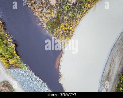 Luftaufnahme der Mündung eines dunklen Flusses und eines schlammigen, hellfarbigen Flusses, umgeben von herbstfarbenen Bäumen und felsigen Ufern in Moose Creek, Ala Stockfoto