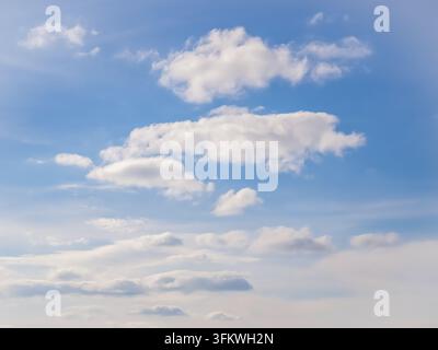 Weiche weiße Wolken, die über einen klaren blauen Himmel verstreut sind, schaffen einen hellen und friedlichen natürlichen Hintergrund. Stockfoto