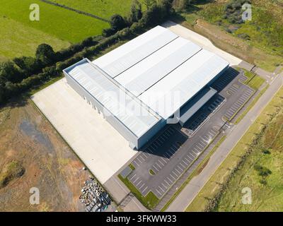 Luftaufnahme eines großen modernen Industriegebäudes mit einem geräumigen Parkplatz, umgeben von grünen Feldern in Lisburn, Nordirland, Einheit Stockfoto