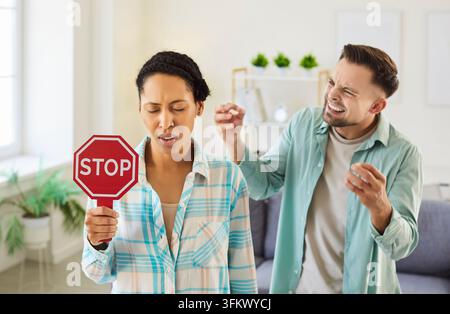 Frau hält ein Stoppschild, während ihr Ehemann während eines hitzigen Konflikts zu Hause auf sie schreit Stockfoto