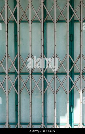 Nahaufnahme eines alten klappbaren Metall-Sicherheitsgitters vor einer verwitterten türkisfarbenen Tür in George Town, Penang, Malaysia. Stockfoto